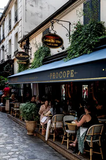 Black and white photo of caf&eacute; tables and chairs evoking Le Procope's old-world interior